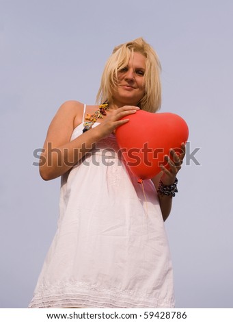 Pretty smiling blonde girl in white dress with red balloon in form of heart