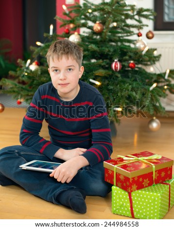 white boy in front of christmas tree with his new tablet pc and other presents