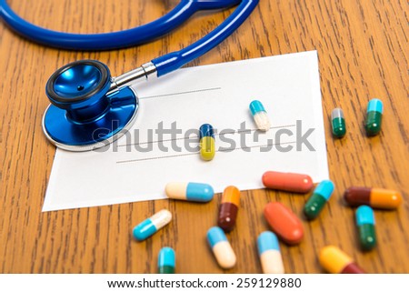 prescription with colorful pills and stethoscope on wooden ground