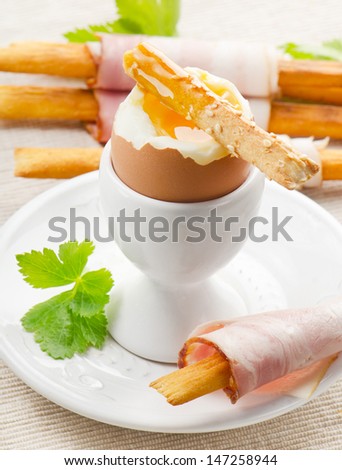 Soft boiled egg in eggcup  with bacon, bread-sticks and herbs