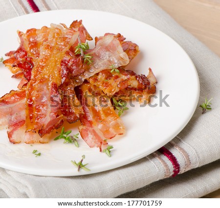 Cooked bacon rashers on a white plate. Selective focus