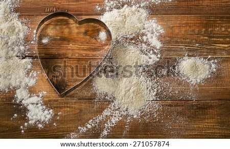 Flour and Heart-shaped cookie cutter on  worn wooden  desk.