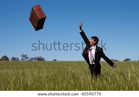 Businessman letting go and release past baggage and instantly enjoys the freedom against a blue sky green grass landscape.