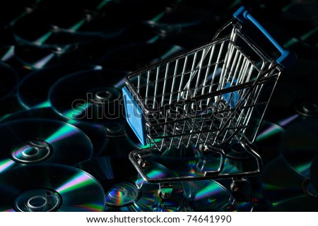 Shopping trolley on a background of CD-ROM DVD CD symbolizing internet or electronic or e-shopping or commerce. Horizontal with large amount of copy space.