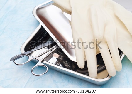 Medical instruments scalpel and clamp in a steel tray with a cover. Medical rubber gloves