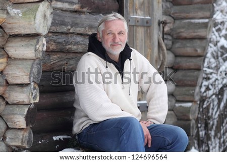 The attractive gray-haired elderly man sits beside log home
