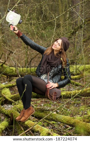 Hipster girl is shooting a film themselves in the woods on a vintage movie camera