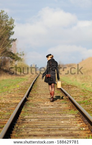 Woman in vintage clothes with a suitcase goes by railway