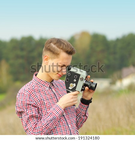 Hipster guy shooting a film on an old vintage movie camera