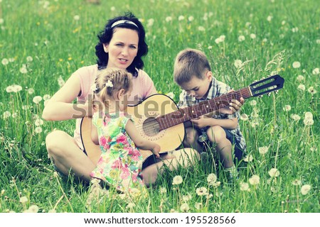 young mother plays the guitar for his young children on nature. happy mother and children playing a vintage guitar outdoors