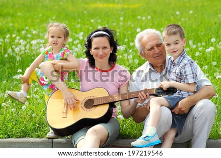 young happy mother playing guitar for her young children and grandfather. romantic portrait of three generations with the guitar.