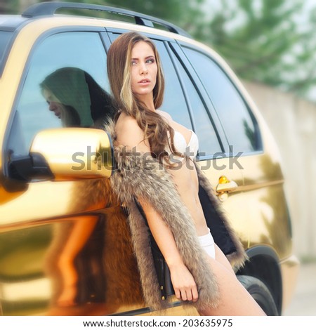 Beautiful sexy girl in bikini and in fur cape posing on a background of golden car. sexy lady near the golden car