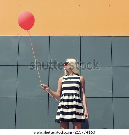 young happy trendy girl stands near a wall mirror with a red balloon. Outdoors, lifestyle. concept of happiness and joy