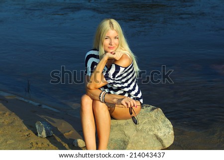 Fashionable beautiful blonde in a striped blouse enjoying on the beach near the water