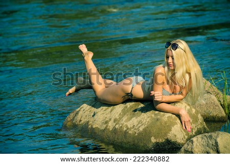 Attractive young blonde woman in a bikini sitting near the water. Pin up girl in vintage toning
