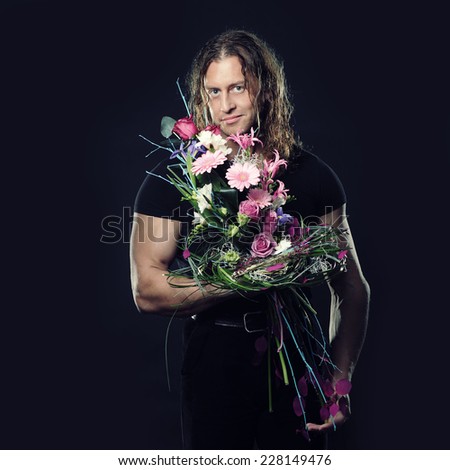 manly muscular man with long hair holds in hands a bouquet of flowers design. Black background.