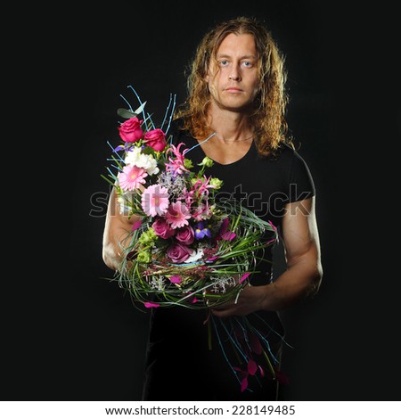 manly muscular man with long hair holds in hands a bouquet of flowers design. Black background.