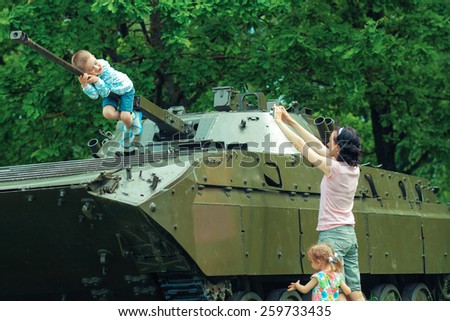 Mom takes pictures of his son on vintage military vehicle.