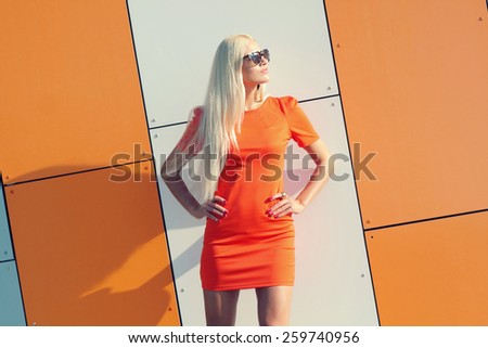 Portrait of trendy fashion girl in sunglasses and in orange dress on the background  of orange wall