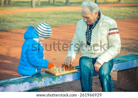 Grandfather and grandson playing chess on a bench outdoors