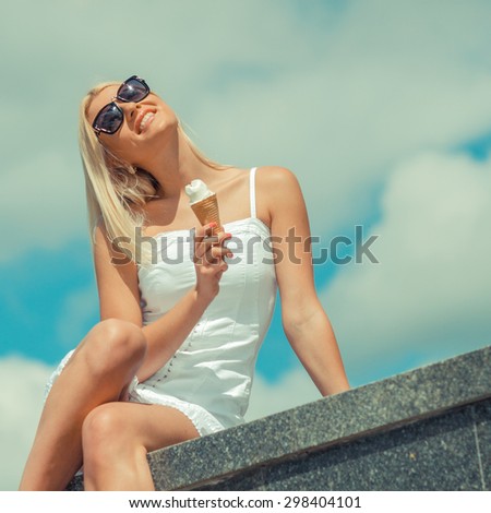 Young sensual girl eating ice cream. Closeup of a pretty woman enjoying an ice cream on the background of cloudy sky. The girl in joyful feelings. Outdoors, lifestyle.