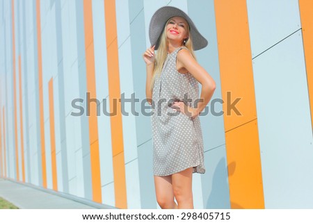 beautiful happy girl in a bright dress and a long hollow hat having fun near the orange wall