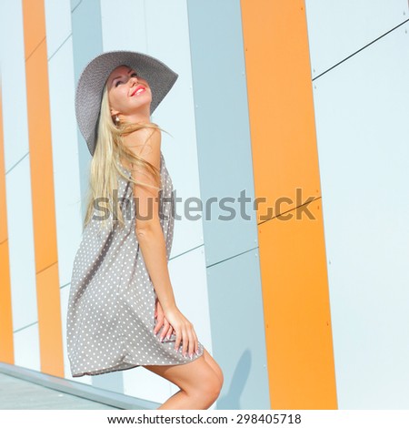 beautiful happy girl in a bright dress and a long hollow hat having fun near the orange wall