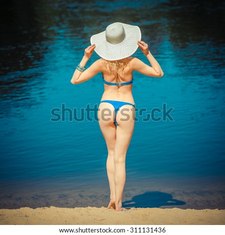 Beautiful female buttocks in bikini from the back. sexy woman buttocks on beach. summer holidays concept - back view of beautiful woman in bikini and a large wide-brimmed hat