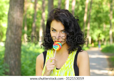 colorful portrait of young sexy funny fashion girl posing  in summer style outfit with red lollipop wearing blue jeans and  t-short. Young sexy girl sucking lollipop. Outdoors, lifestyle.