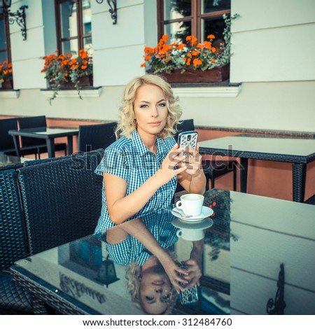 beautiful young girl resting in a cafe. attractive blond model sitting with a cup of coffee in an outdoor cafe of the European city and talking on the phone