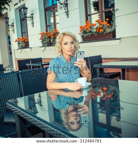 beautiful young girl resting in a cafe. attractive blond model sitting with a cup of coffee in an outdoor cafe of the European city and talking on the phone