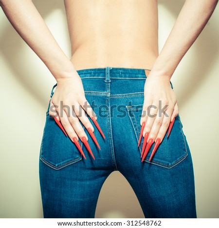 Hands with long red nails on the buttocks in jeans. Young woman with  gel nails manicure holding hand at jeans back
