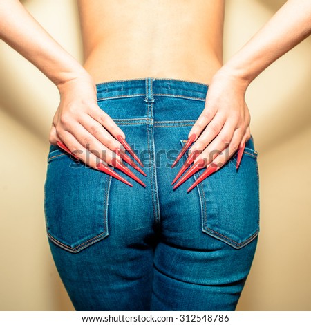 Hands with long red nails on the buttocks in jeans. Young woman with  gel nails manicure holding hand at jeans back