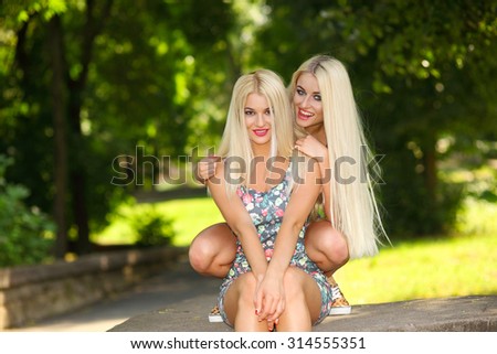 two cheerful blonde girlfriends having fun and fooling around on the street in the city. Two lovely girl friends hugging and having fun.