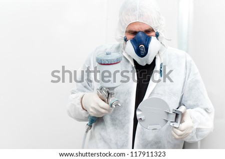 auto worker painting a car body component with spray gun