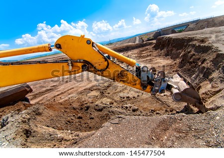 Industrial excavator moving earth and loading a dumper truck on road construction site