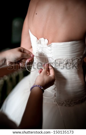 Maid of honor helping the bride to put her wedding dress on by tying the back bow. helping to lace up bride\'s wedding dress