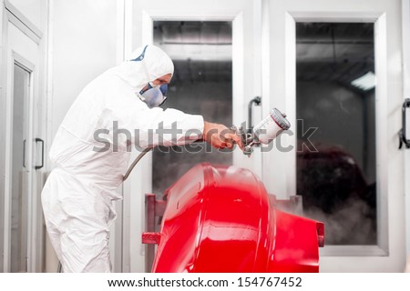 car painter working on a red car in a special painting booth
