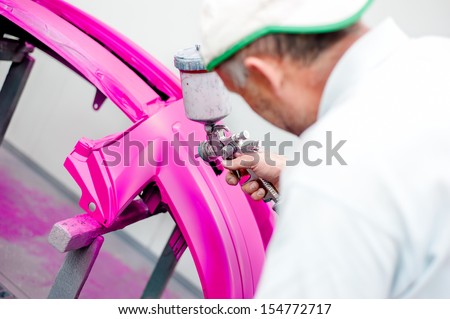 man painting a purple bumper of a car in special booth with airbrush