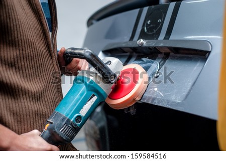 professional mechanic cleaning the metal surface of the bodywork of a car with power buffer machine. Polish procedure and car care concept