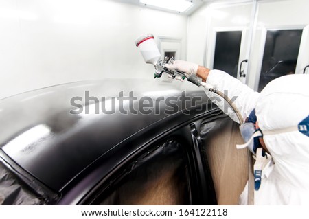 qualified worker spraying black paint on a car in special painting booth