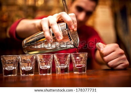 barman hand with shake mixer pouring beverage into glasses on bar