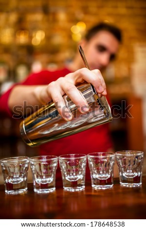 Close-up of Barman pouring alcoholic drink and cocktails into small glasses on bar counter