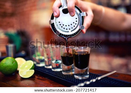 barman mixing and pouring a summer alcoholic cocktail into small, shot glasses on counter