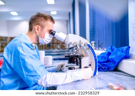 Scientist working in chemistry laboratory, examining samples at microscope