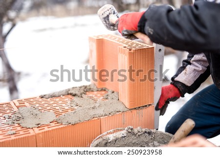 Man on construction site working with bricks and mortar, building house walls on winter