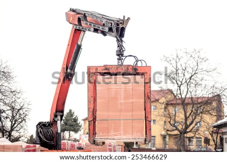 Crane delivers a brick pallet at building construction site, isolated on white sky