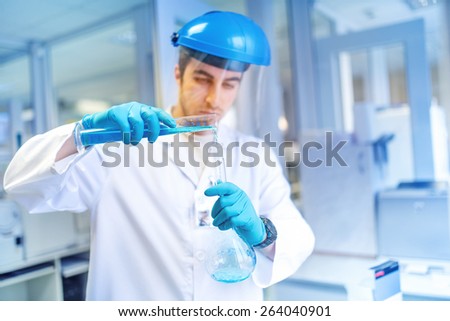 young male scientist learning and making experiments in chemical laboratory with liquid substances