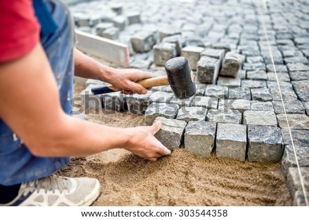 Construction worker installing stone blocks on pavement, street or sidewalk construction works