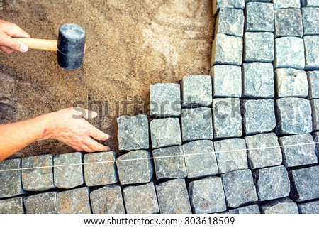 industrial worker installing pavement rocks, cobblestone blocks on road pavement